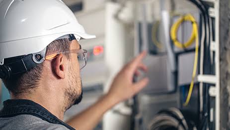 Technician with hard hat and safety glasses working inside a low-voltage control panel