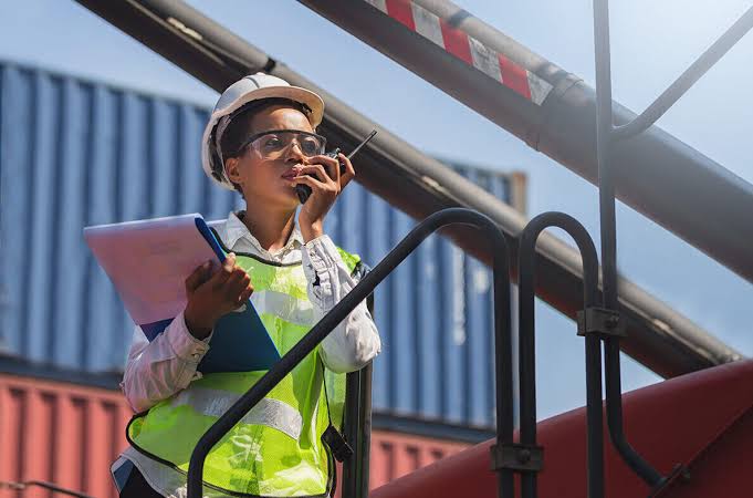Field inspector with hard hat and two-way radio coordinating at a port and logistics facility