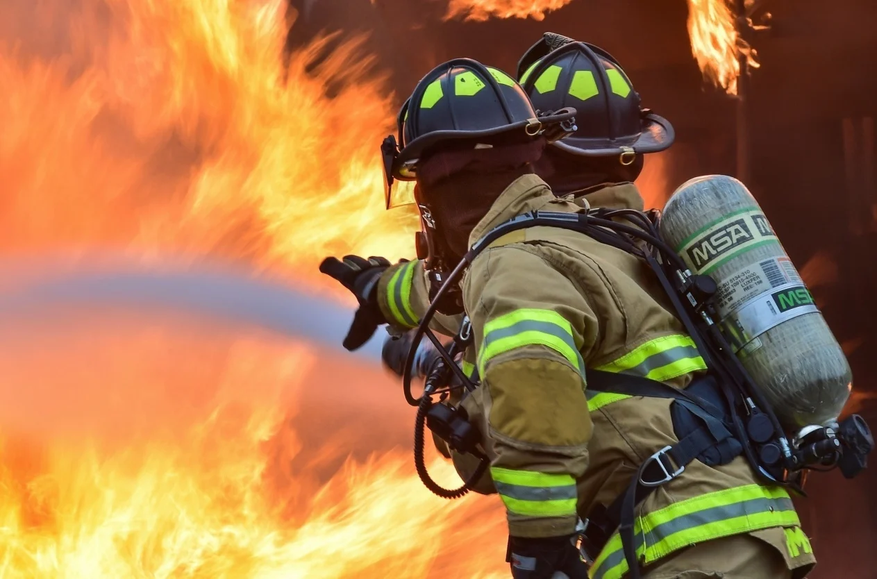Two firefighters in full turnout gear advancing a hose line into a structure fire